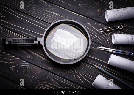 Magnifier, bussole e rulli dal disegno su un nero lo sfondo di legno Foto Stock