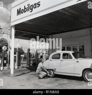 Degli anni Cinquanta, storico i giorni d'oro dell'automobilismo, una stazione di servizio sttendant controlla la pressione di gonfiaggio dei pneumatici su una Austin auto parcheggiate al Mobilgas Ravenscroft stazione di servizio, Great West Road, Londra, Inghilterra, Regno Unito. Foto Stock