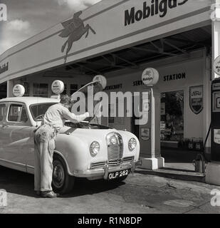 Degli anni Cinquanta, storico i giorni d'oro dell'automobilismo, una stazione di servizio sttendant controlla l'olio su una Austin auto parcheggiate presso le pompe di benzina al Mobilgas Ravenscroft stazione di servizio, Great West Road, Londra, Inghilterra, Regno Unito. Foto Stock