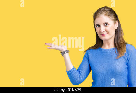 Bella la mezza età coppia donna che indossa un maglione invernale su sfondo isolato sorridente allegro presentando e dispositivo di puntamento con il palmo della mano in cerca di un Foto Stock