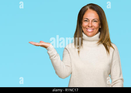 Bella la mezza età adulto donna che indossa un maglione invernale su sfondo isolato sorridente allegro presentando e dispositivo di puntamento con il palmo della mano guardando Foto Stock