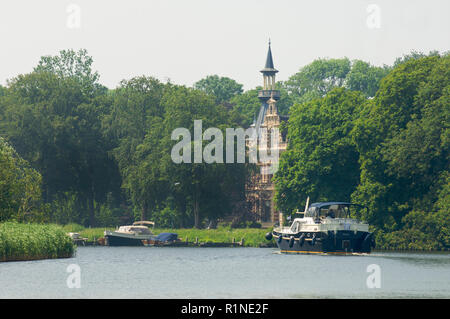 Uno yacht che viaggiano sul fiume de Vecht passando una magione classica con piccole imbarcazioni parcheggiata di fronte alla casa, Paesi Bassi Foto Stock