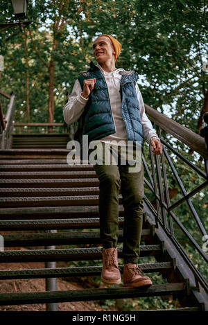 Giovane turista elegante blogger in arancione hat è sui gradini del parco nazionale. Vista posteriore, stagione primaverile, libero stile casual Foto Stock