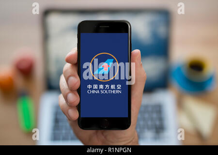 Un uomo guarda al suo iPhone che visualizza la China Southern Airlines logo, mentre se ne sta seduto alla sua scrivania per computer (solo uso editoriale). Foto Stock