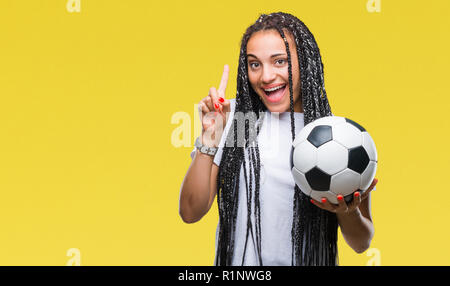 Giovani capelli intrecciati African American Girl tenendo palla calcio su sfondo isolato sorpreso con un'idea o domanda puntare il dito con felice fa Foto Stock