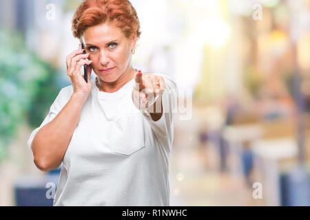 Accattivante senior redhead caucasica donna parlando sullo smartphone su sfondo isolato puntando con il dito per la telecamera e a voi, mano segno, pos Foto Stock