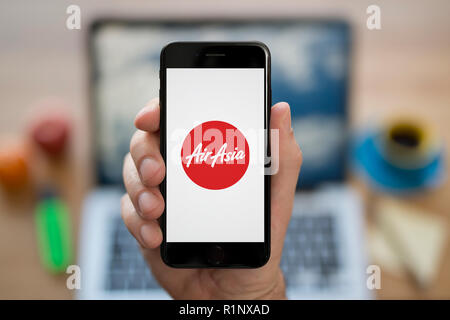 Un uomo guarda al suo iPhone che visualizza la Air Asia logo, mentre se ne sta seduto alla sua scrivania per computer (solo uso editoriale). Foto Stock