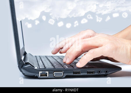 Il cloud computing concetto che mostra le mani la digitazione sulla tastiera del computer con Internet comune icone multimediali sotto le nuvole da lo schermo del laptop. Foto Stock
