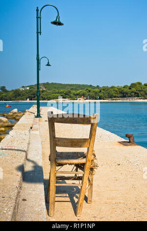 Vecchia sedia in legno su un molo di fronte la spiaggia Koukounaries, mattina all' isola di Skiathos, Grecia Foto Stock