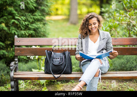 La ragazza seduta su una panchina, la lettura di un libro Foto Stock