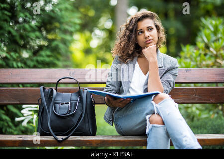 La ragazza seduta su una panchina, la lettura di un libro Foto Stock