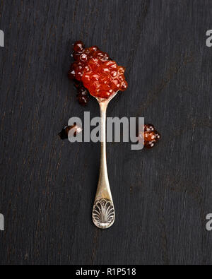 Caviale rosso in un cucchiaio su nero lo sfondo di legno Foto Stock