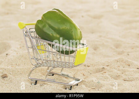 Il verde di peperone dolce paprika nel carrello della spesa standingon sabbia. Peperone verde sul carrello per vendere. Caricato vegetale in una miniatura del carrello Foto Stock