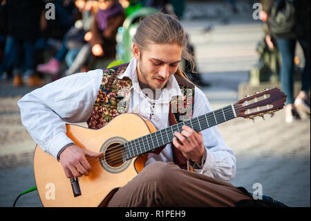 Cracovia in Polonia: un suonatore ambulante suona la chitarra nella piazza del vecchio mercato. Sorridente, seduto musicista esegue su una chitarra acustica ad una folla di persone. Foto Stock