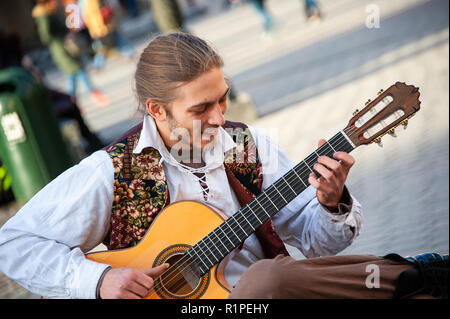 Cracovia in Polonia: un suonatore ambulante suona la chitarra nella piazza del vecchio mercato. Sorridente, seduto musicista esegue su una chitarra acustica ad una folla di persone. Foto Stock