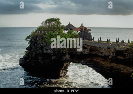 Tempio chimerico sull'acqua. Tempio di acqua in Bali. Indonesia natura paesaggio. Famoso punto di riferimento di Bali. Gli spruzzi delle onde e pietra. Giorno nuvoloso in Indonesia. Acqua e rocce prima della tempesta Foto Stock