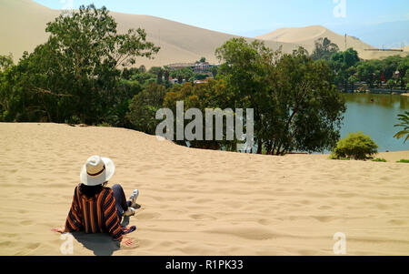 Rilassante femmina sulla duna di sabbia, ammirando la città oasi di Huacachina, Ica, Perù Foto Stock