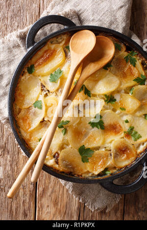 Cucina finlandese Janssonin Kiusaus. Patate al forno con le acciughe, cipolle e crema di latte in una padella. Verticale in alto vista da sopra Foto Stock