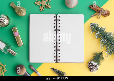 Creative laici piana di imbarcazioni e notebook vuoto mock up con ornamenti natale e costituiscono elementi di bellezza sul verde e sfondo giallo, vista superiore con Foto Stock