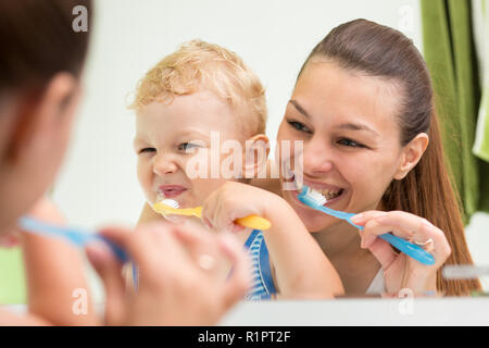 Madre bella aiutando il suo bambino figlio di spazzola denti nella stanza da bagno Foto Stock