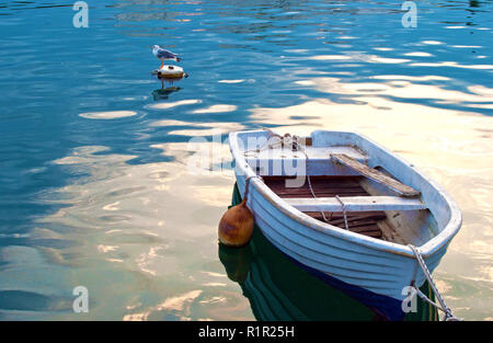 Una vecchia barca bianca galleggiante nel mare blu dell'acqua. Uno bianco e grigio seagull sulla schiena seduta su una boa. Tranquilla e calma atmosfera mattutina Foto Stock