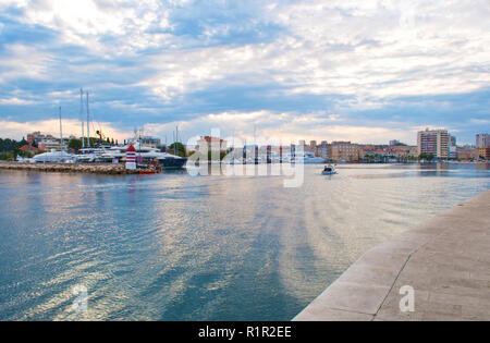 Una piccola barca in acqua di mare sul suo modo al marine contro lo sfondo della graziosa piccola gialla case. La città di Zadar, Croazia Foto Stock