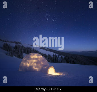 Paesaggio notturno con un igloo di neve con la luce. Casa estreme. Inverno in montagna. Il cielo con le stelle Foto Stock