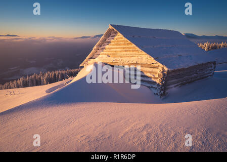 Paesaggio invernale con capanne di legno in montagna. Mattina di sole. Grande cumulo di neve Foto Stock