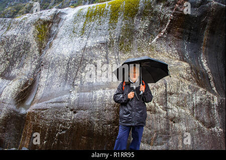 L'uomo ripari sotto ombrellone, contro la parete di roccia liscia, colorato, moss coperte di sfondo di roccia in Franz Josef National Park, Nuova Zelanda Foto Stock