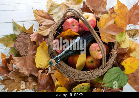 Foglie di autunno con una bottiglia di sidro di mele e le mele nel cestino Foto Stock