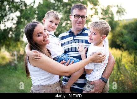 Una giovane famiglia con due figli piccoli in piedi all'aperto in natura in un giorno di estate. Foto Stock