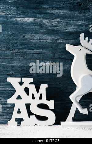 Il tridimensionale di parola xmas, abbreviazione per Natale e un bianco di renne di legno contro un rustico grigio superficie in legno con un po' di spazio vuoto su Foto Stock