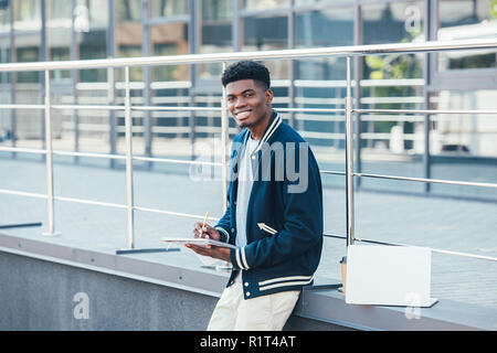 Sorridente African American freelance lavoro con documenti in città con il computer portatile Foto Stock