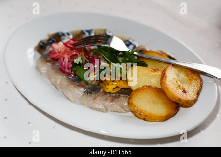 Ristorante piatto - patate al forno con anelli di cipolla e di aringa su una piastra bianca in un ristorante Foto Stock