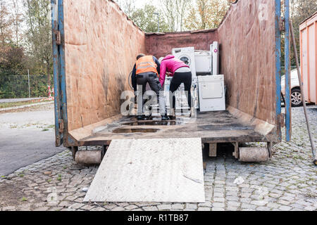 Donna e uomo dando elettrodomestici al centro di riciclaggio di una macchina di lavaggio Foto Stock