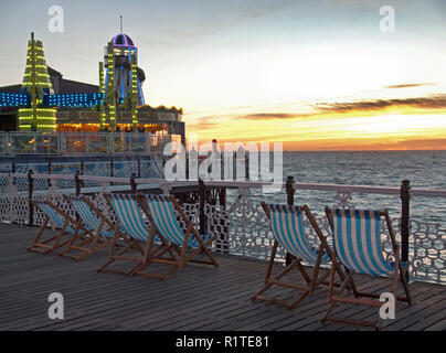 Sedie a sdraio di fronte al tramonto sul molo di Brighton Foto Stock