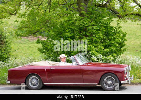 Automobilista la guida 1961 British realizzato Alvis TD21 serie DHC 1 drophead ooupe classic car sul paese lane in Cotswolds, Inghilterra Foto Stock