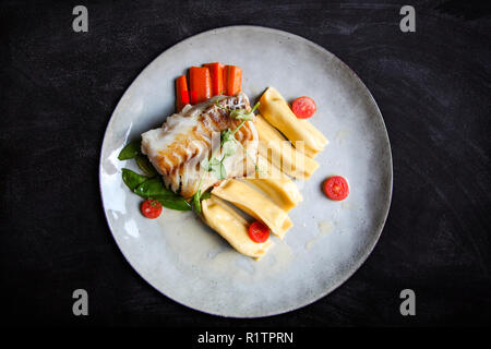 Estetica di filetto di merluzzo bianco servito con gnocchi di patate, carote, verde pisello dolce e pomodori al ristorante vegetariano Foto Stock