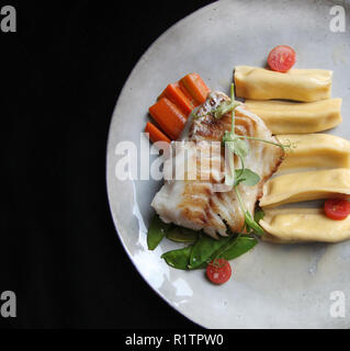 Estetica di filetto di merluzzo bianco servito con gnocchi di patate, carote, verde pisello dolce e pomodori al ristorante vegetariano Foto Stock