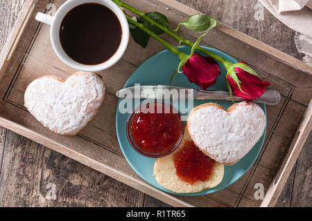 Il giorno di San Valentino la prima colazione con caffè, a forma di cuore bun, marmellata di frutti di bosco e le rose su un vassoio. Vista superiore Foto Stock