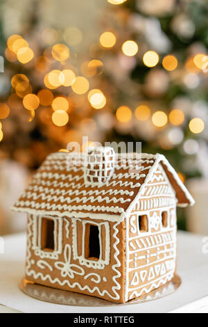 Gingerbread house sulla tabella. Luci sfocati di albero di Natale. In mattinata il luminoso soggiorno. Atmosfera natalizia. Foto Stock