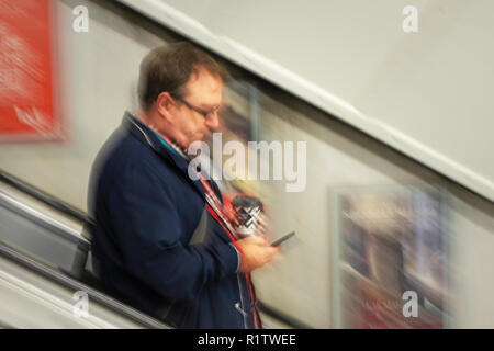 Tubo tempo di pendolari, Londra " commuter " maschio che si muove in basso lungo le scale mobili della metropolitana Foto Stock