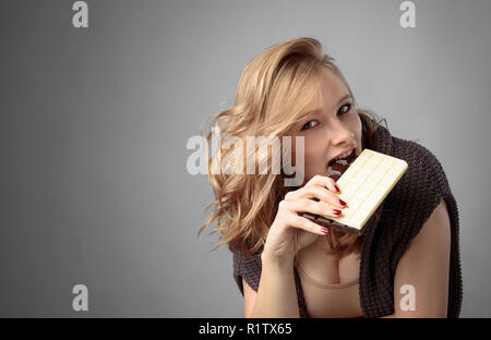 Felice giovane bella donna di mangiare cioccolato. Giovane biondo con trucco naturale divertendosi e mangiando cioccolato. Foto Stock