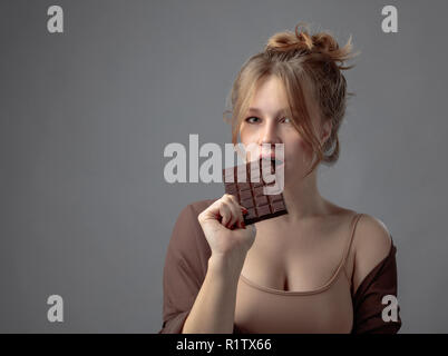 Felice giovane bella donna di mangiare cioccolato. Giovane biondo con trucco naturale divertendosi e mangiando cioccolato. Foto Stock