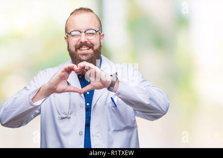 Giovane medico caucasica uomo che indossa medical mantello bianco su sfondo isolato sorridente in amore che mostra il simbolo del cuore e la forma con le mani. Romantico con Foto Stock