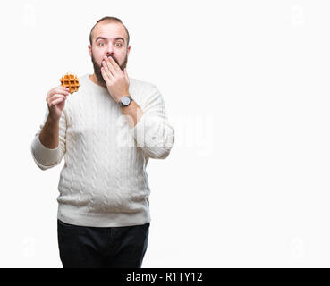 Giovani caucasici uomo parigamba mangiare dolci waffle su sfondo isolato coprono la bocca con la mano sconvolto con vergogna per errore, espressione di paura, sca Foto Stock