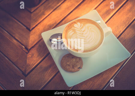 Bel mattino tavolo in legno top con caffè, latte art e cookie. Per iniziare la giornata, buon umore concetto. Foto Stock