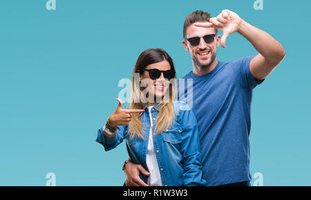 Coppia giovane in amore indossando occhiali da sole su sfondo isolato sorridente rendendo il telaio con le mani e le dita con la faccia felice. Creatività e fotografi Foto Stock