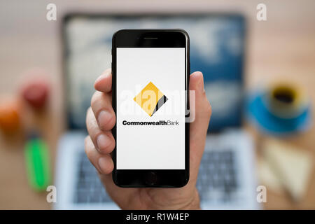 Un uomo guarda al suo iPhone che visualizza il Commonwealth Bank logo, mentre se ne sta seduto alla sua scrivania per computer (solo uso editoriale). Foto Stock