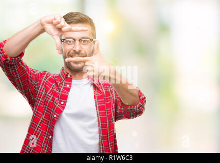 Giovane uomo bello su sfondo isolato sorridente rendendo il telaio con le mani e le dita con la faccia felice. La creatività e il concetto di fotografia. Foto Stock